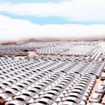 Thousands of white cars lined up in neat rows across a desert parking lot, stretching to the horizon.