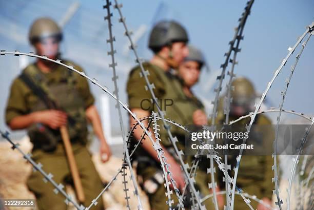 i a - Center News Network Barbed wire in the foreground with blurred soldiers in combat gear standing behind, suggesting a military checkpoint or border area.