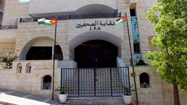 Facade of the Journalists Syndicate building (نقابة الصحفيين) with two Jordanian flags, a metal gate, and steps leading up to the entrance.