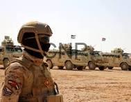 jaish - Center News Network Frontline view of a soldier in desert camouflage and helmet, with a line of armored trucks in a dusty training area behind him.