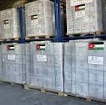 Row of gray metal shipping containers on wooden pallets in a warehouse, with blue racks in the background.