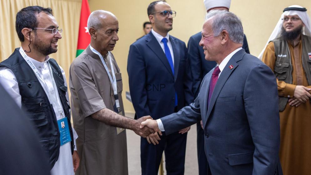 kinghoj - Center News Network Group of men in formal and traditional attire shake hands at a diplomatic event, with a Jordan flag in the background.