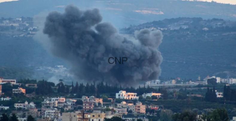 Massive dark smoke plume rising from a blast over a town, with houses in the foreground and hills in the background.