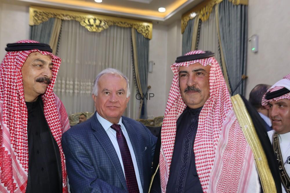 maan1 - Center News Network Three men in traditional red-and-white keffiyehs flank a suited man at a formal event indoors with gold decor in the background.