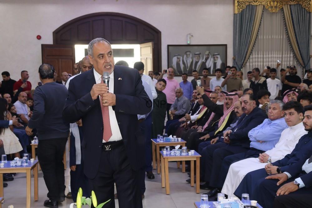 A man in a suit speaks into a microphone at a formal gathering, addressing a seated audience in a large hall.