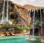Resort with multiple waterfalls cascading into a turquoise pool, lounging area under a thatched canopy, and cliffs in the background.