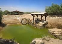 magh - Center News Network Rural scene with a small wooden pavilion over a green pond in a dry, tree-spattered landscape under a blue sky.