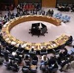 Roundtable conference with numerous delegates seated around a circular table; a central piano/speaker area at the middle.