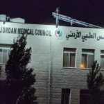 Night view of the Jordan Medical Council building with English and Arabic signage on a white stone wall.