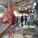 mas - Center News Network Person holding a slaughtered animal carcass in a busy meat market or processing area, with workers in the background.