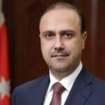 Portrait of a man in a navy suit and red tie, with a Turkish flag in the background.