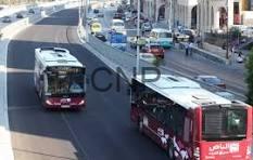naqqq - Center News Network Two red city buses travel along a busy urban street with cars and pedestrians nearby.