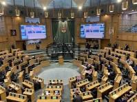 Parliament chamber with a central podium and semicircular rows of desks, flanked by large screens displaying information.