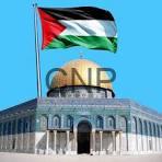 Palestinian flag flies above a historic stone building with arched entrance against a bright blue sky.