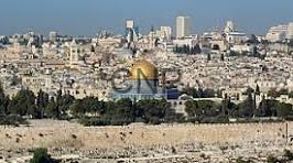 quds - Center News Network Wide view of a historic city with white stone buildings and ancient walls, set against a dry rocky foreground and blue sky.