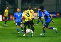 ramtha - Center News Network Soccer match: a yellow jersey player controls the ball while blue-jersey opponents converge on a green field under stadium lights.