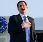 Man in a dark suit giving a speech at a podium, hand over heart, with a government seal visible in the background.
