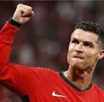 Soccer player in a red jersey raising a clenched fist in celebration on the field.
