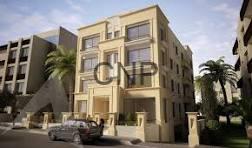 Three-story beige apartment building with balconies on a sunny street, palm trees in front and parked cars nearby.