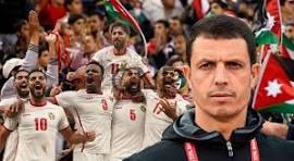 sal - Center News Network Serious coach in the foreground as a men's soccer team celebrates in white jerseys with red numbers in the background, flags visible in the stands.