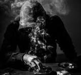 tad - Center News Network A person in a suit sits at a table in a dark, smoky scene with a skull in front of them.