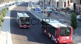 tra - Center News Network Red tram in the foreground travels along a city street while a white tram and cars pass by, storefronts lining the sidewalk behind.