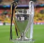 Silver trophy on a green football field with a blurred stadium in the background, ribbons hanging from the handles.