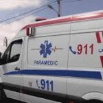 White ambulance with red and blue stripes and 911/Paramedic markings parked on a street, Arabic text visible on the side, suggesting emergency medical services.