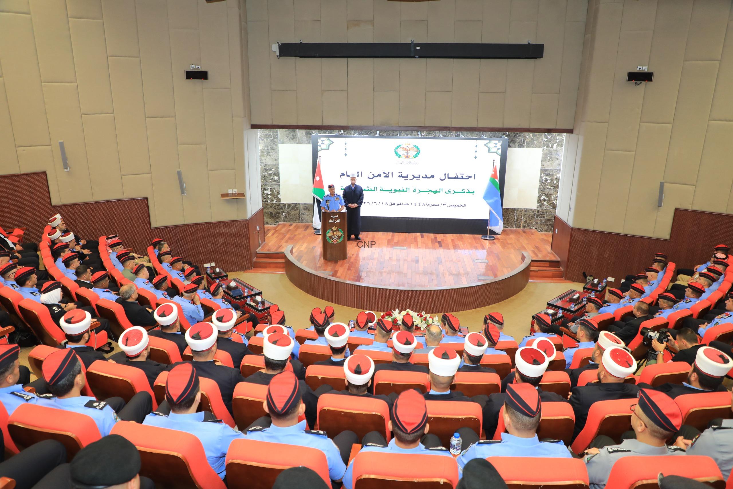 Formal ceremony in an auditorium with uniformed officers seated in red chairs, speakers at a podium on a stage with a large banner behind them.