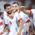 Jordanian national football team players celebrate a goal on the field, smiling and embracing each other.