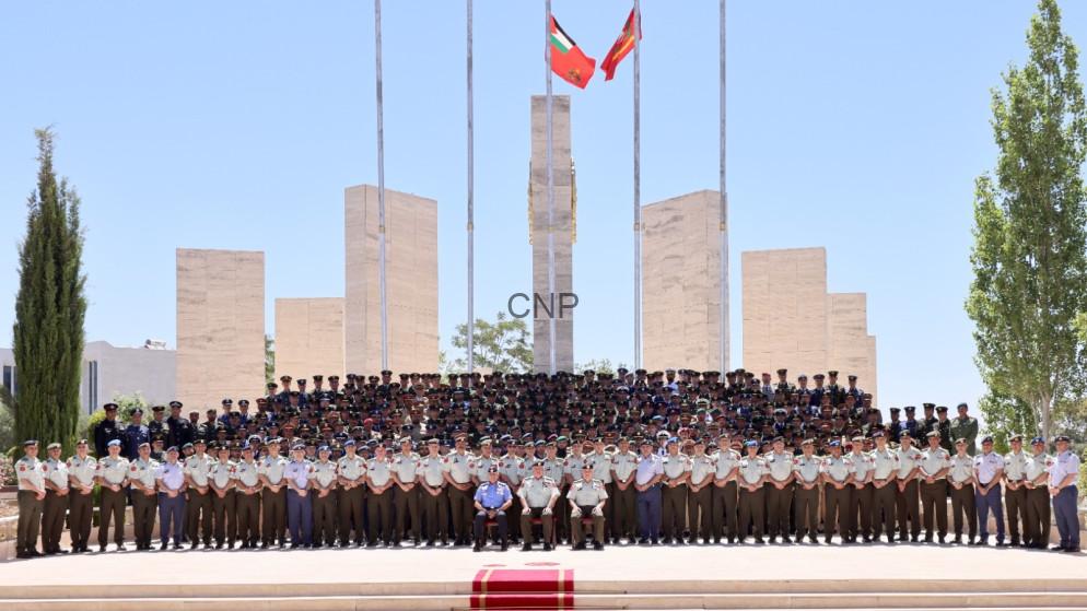 Large group of uniformed military personnel posing for a formal group photo in front of a stone monument with flags flying overhead.