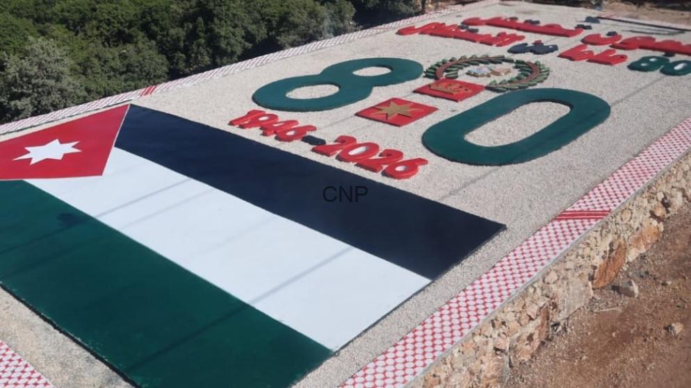 Outdoor memorial slab featuring the Jordan flag, large green numerals, and a red-and-white patterned border on a gravel surface.