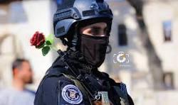 amen - Center News Network Tactical police officer in helmet and balaclava with a red rose near the shoulder, contrasting force and gentleness as a symbolic moment.