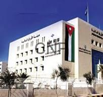 Modern white institutional building with Arabic signage, palm trees, and a Jordan flag on a flagpole in front.