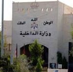 Front view of a beige building with Arabic signage and emblem on the facade, surrounded by trees; a black-and-white portrait poster appears on the right side.