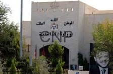 Front view of a beige building with Arabic signage and emblem on the facade, surrounded by trees; a black-and-white portrait poster appears on the right side.