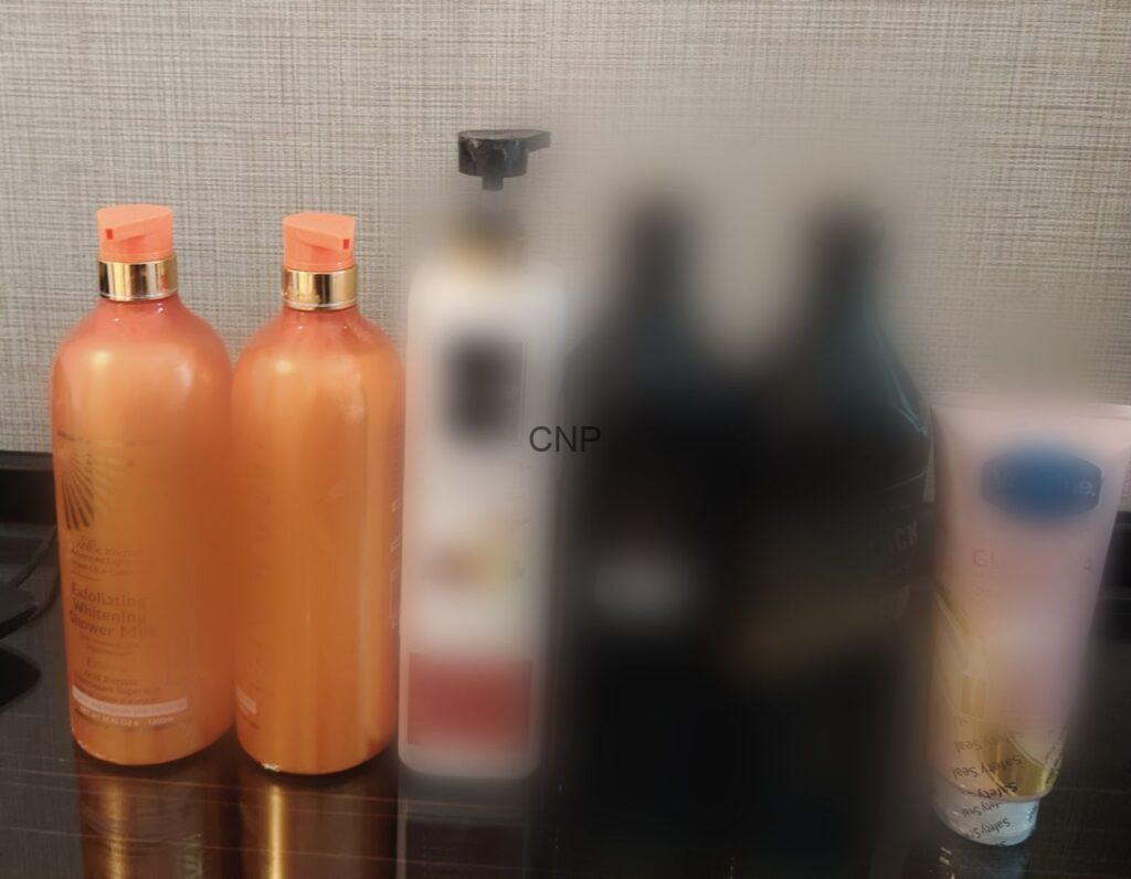 Three orange pump bottles on a bathroom shelf with blurred background bottles behind them.