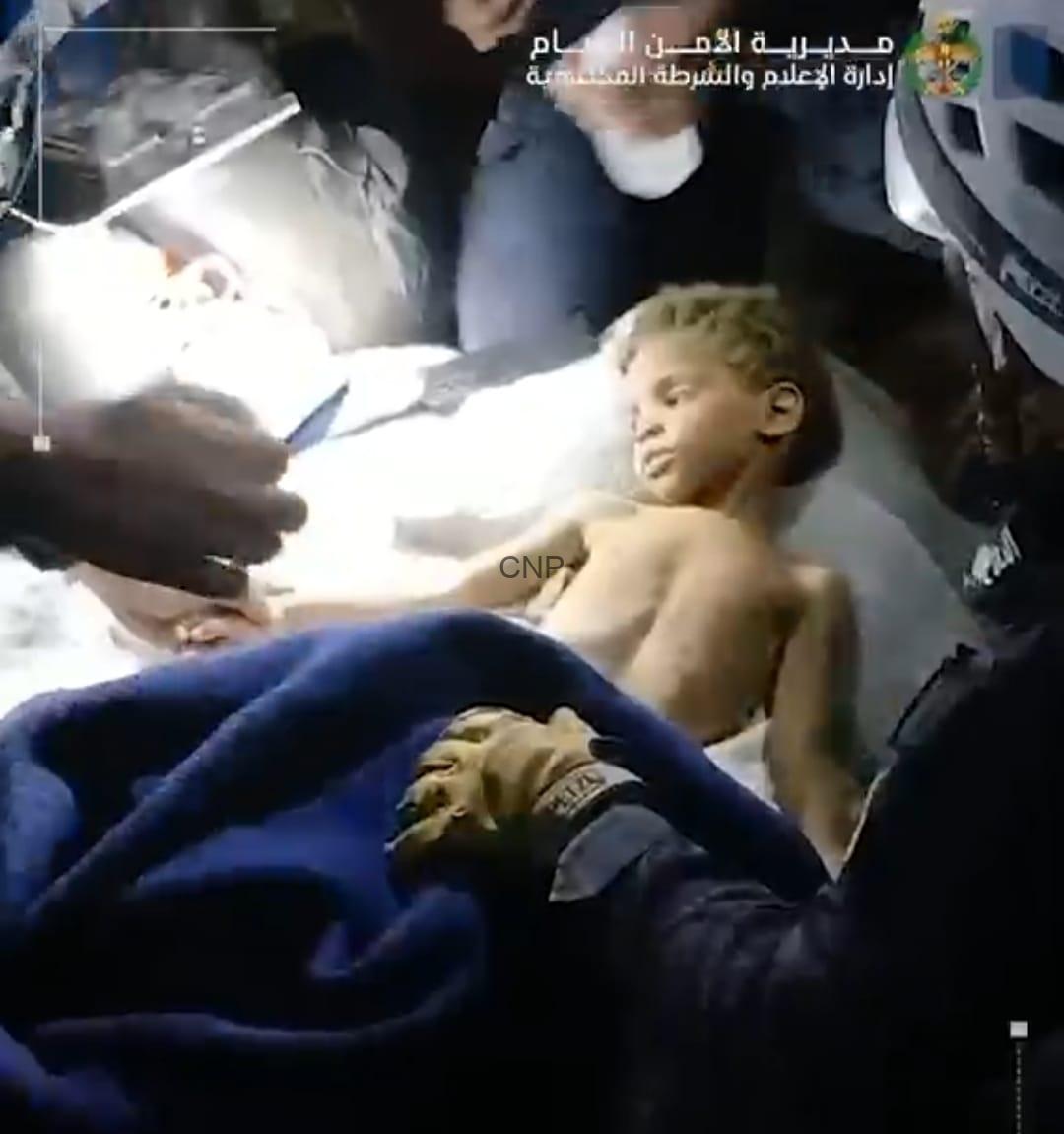 fan4 - Center News Network Boy lying shirtless on a hospital bed while medical staff attend to him in an emergency setting, bright light overhead.