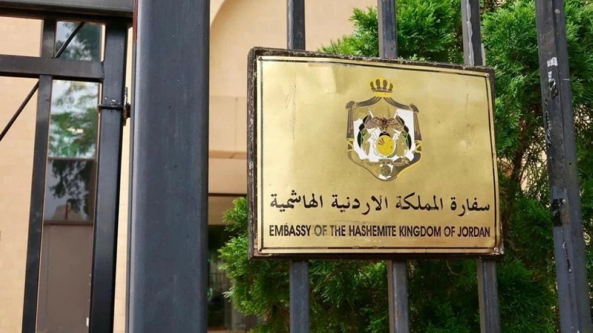 Brass plaque on a black gate reading 'Embassy of the Hashemite Kingdom of Jordan' with the Jordanian coat of arms above the text (Arabic and English).