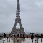 Eiffel Tower centered in view with crowds of people on a damp plaza under gray, cloudy skies.