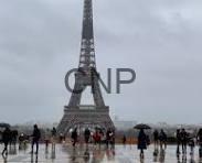 Eiffel Tower centered in view with crowds of people on a damp plaza under gray, cloudy skies.