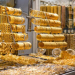 Gold jewelry display with stacked bracelets, bangles, and necklaces in a shop window.