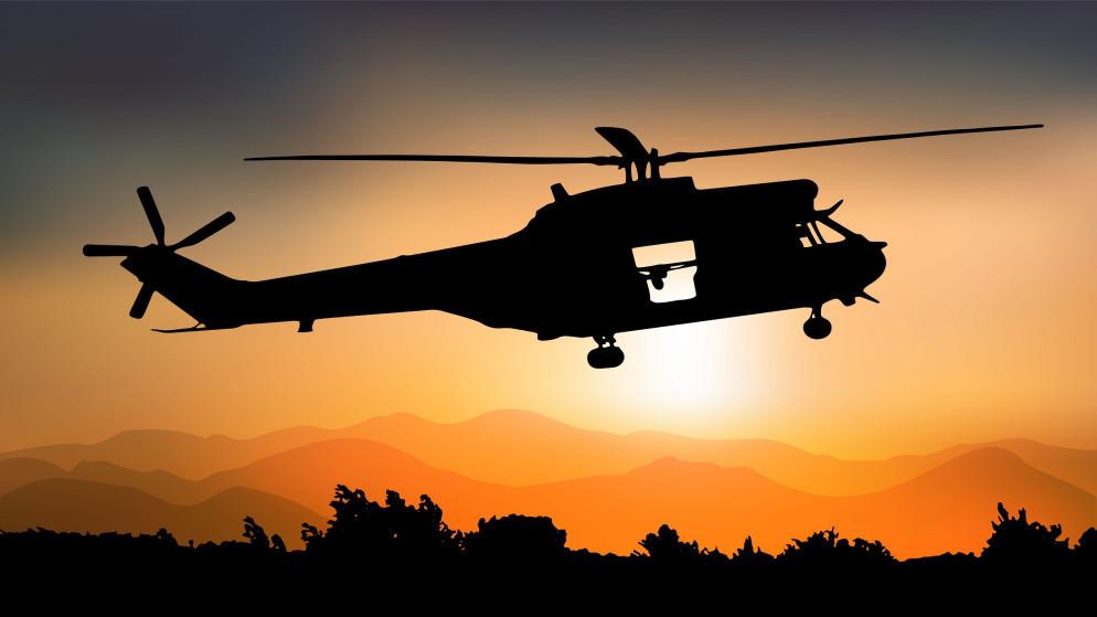 Silhouette of a helicopter flying at sunset over a ridge and trees at dusk.