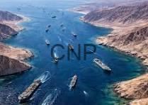 Aerial view of a busy shipping canal with several cargo ships moving through turquoise water between steep brown cliffs.