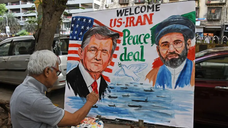 Street artist painting a large outdoor mural promoting a US–Iran peace deal, with two portrait figures and the words 'Peace deal' above water scene.