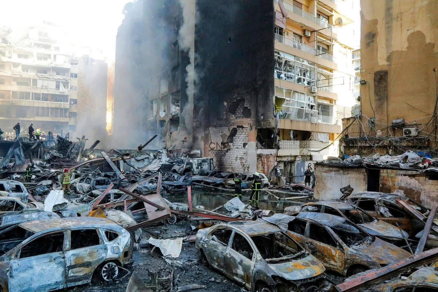 jnob - Center News Network Firefighters amid charred ruins and collapsed cars in a destroyed urban block after a disaster.