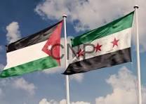 Two national flags waving in the wind: Jordan on the left and Syria on the right, against a blue sky with scattered clouds.