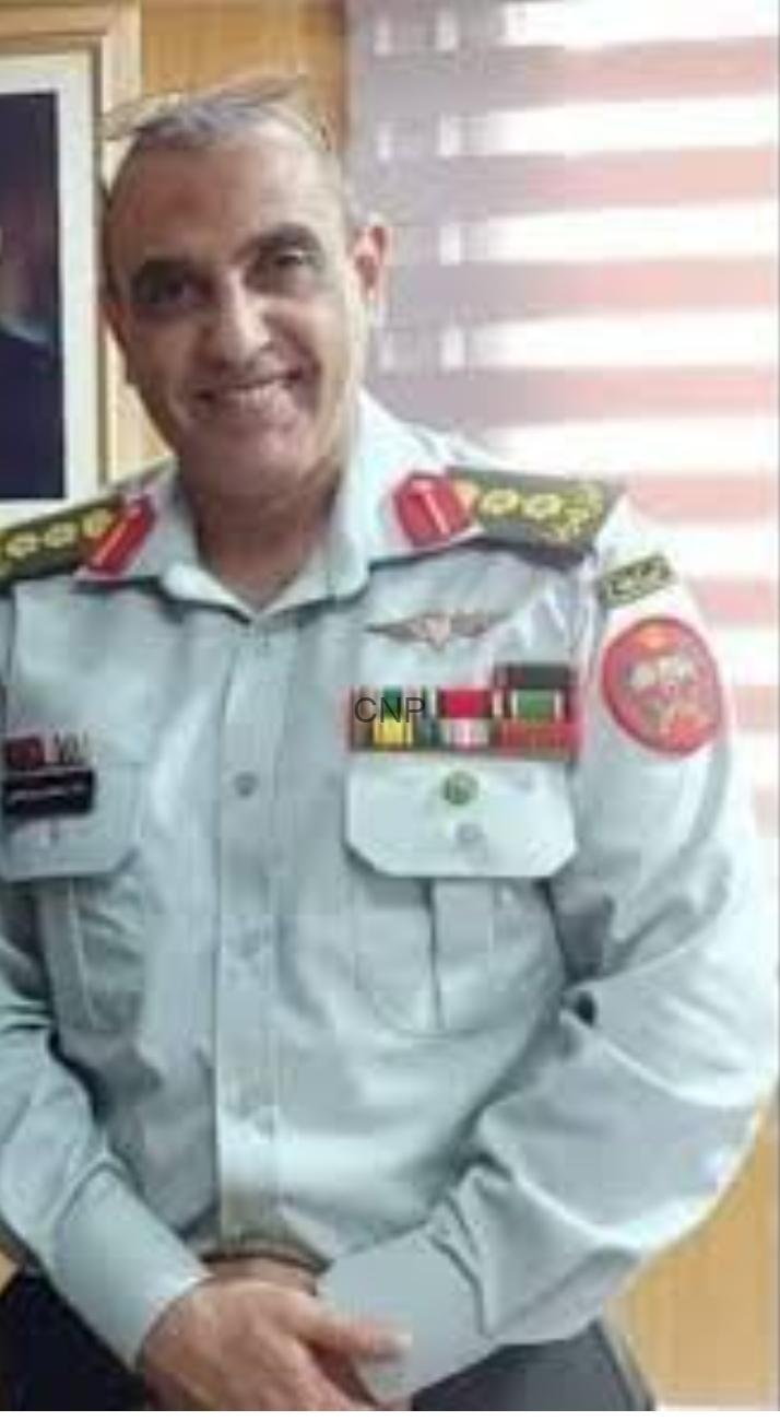 khal - Center News Network Smiling man in a light gray uniform with ribbons and patches, posing indoors.