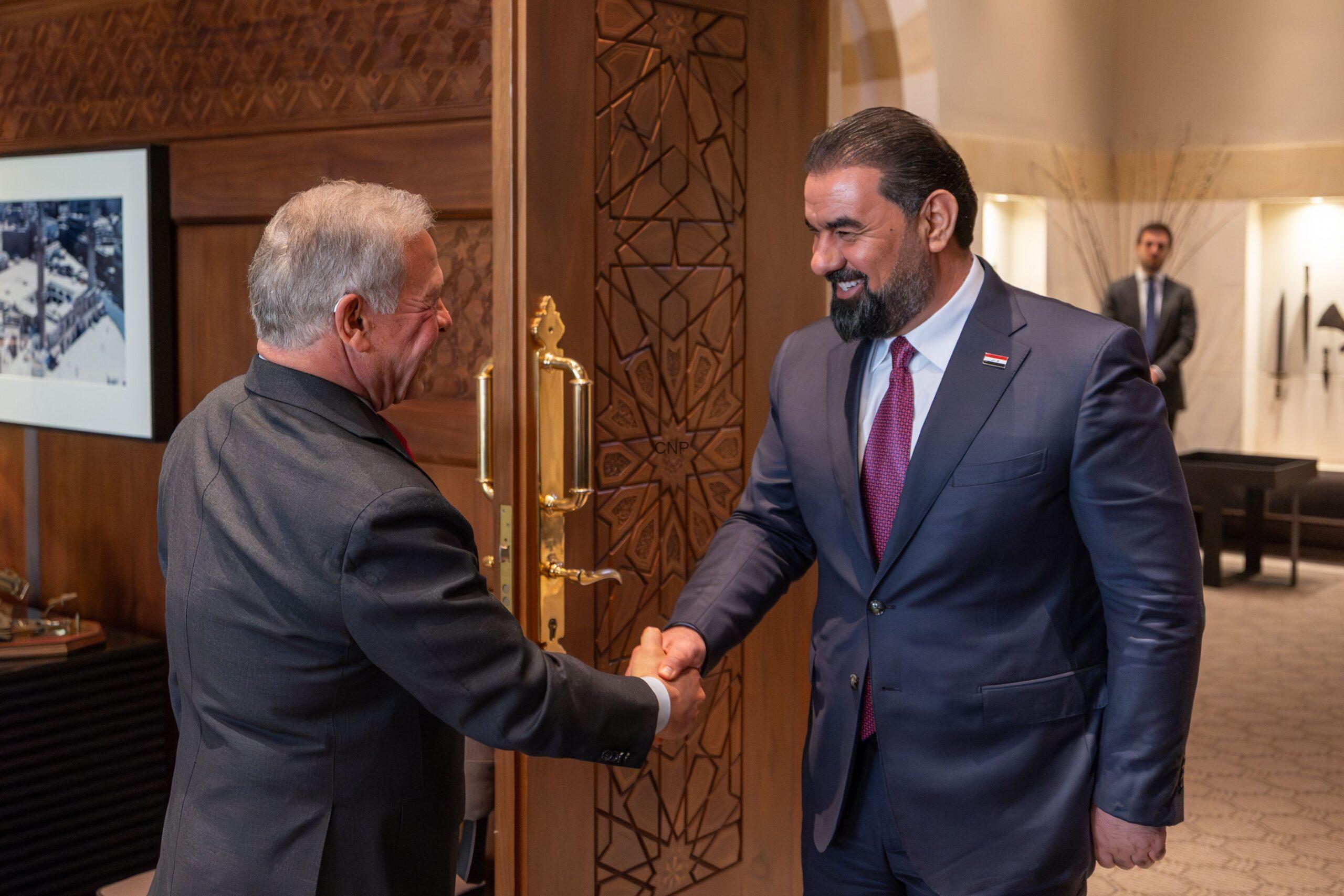 kinira - Center News Network Two men in suits shake hands at a carved wooden door in a formal lobby setting.