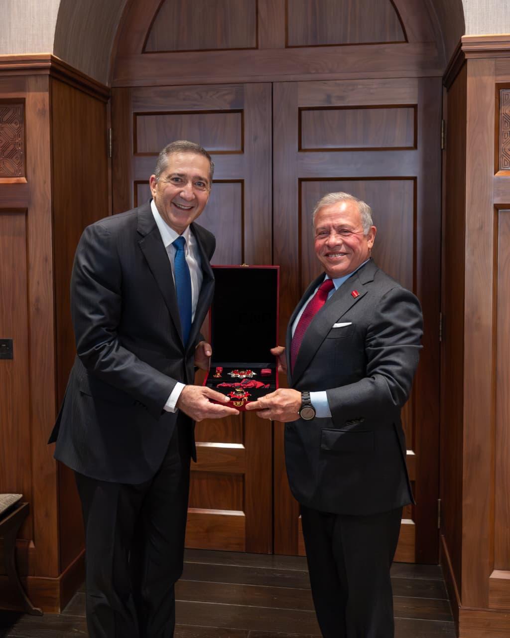 kinsa - Center News Network Two men in suits exchange a red velvet medal box, smiling, in a wood-paneled room.